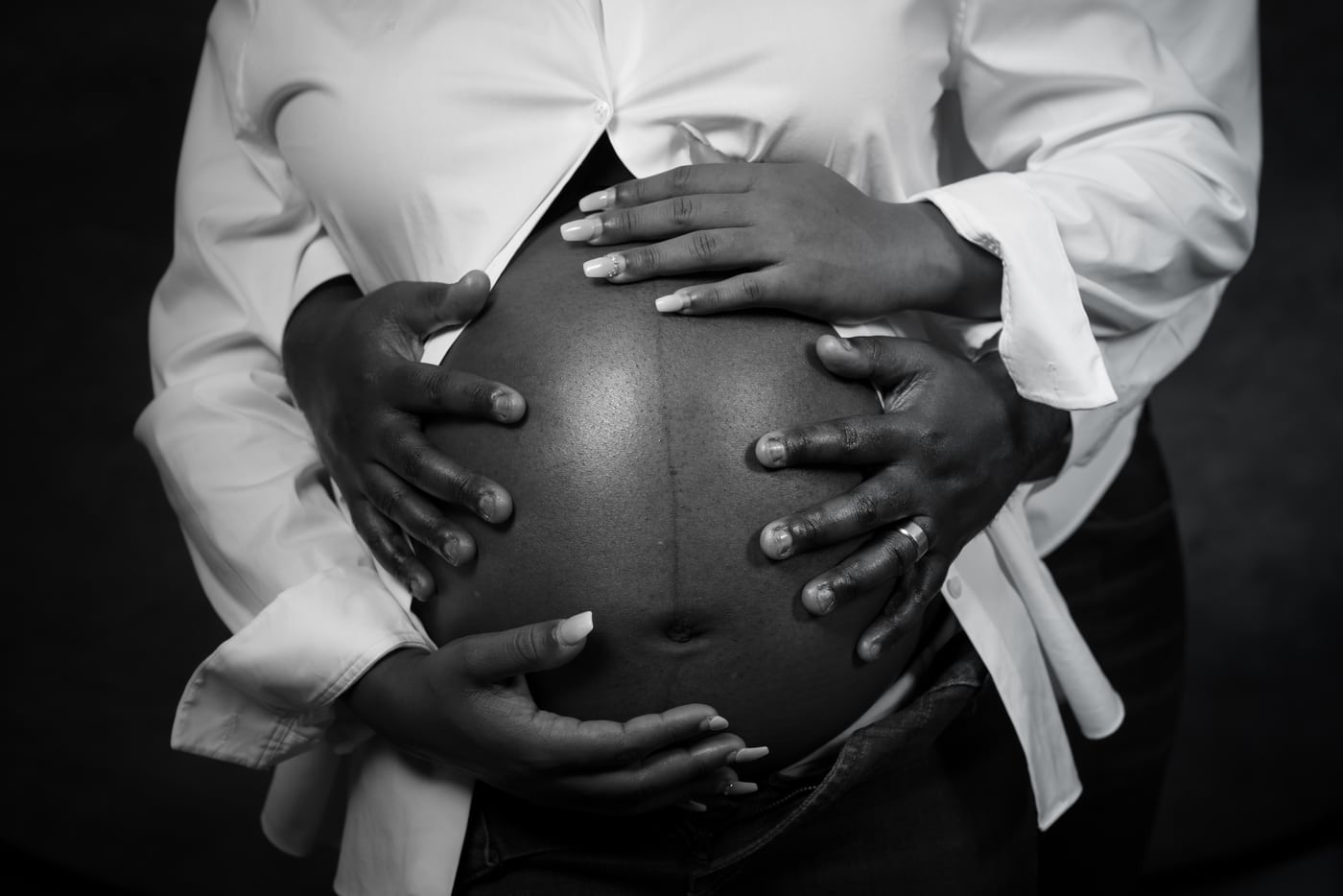 Both partners' hands on belly, B&W, tender detail.