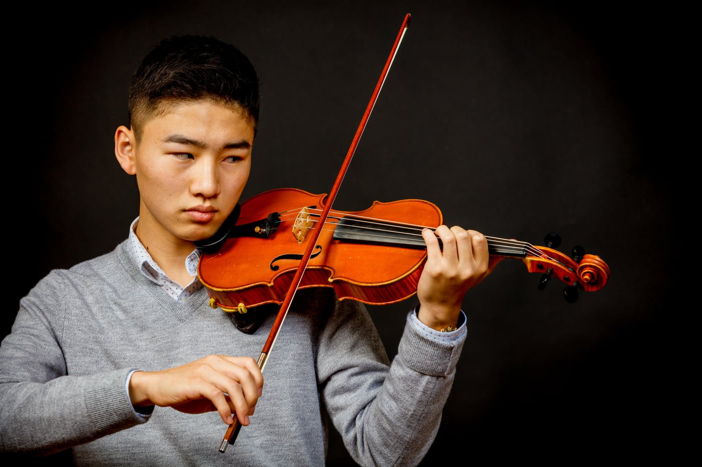 Young man playing violin, dark bg, music portrait.