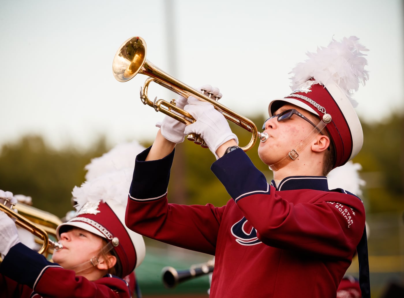 Marching band trumpets, plumes, band/motion.