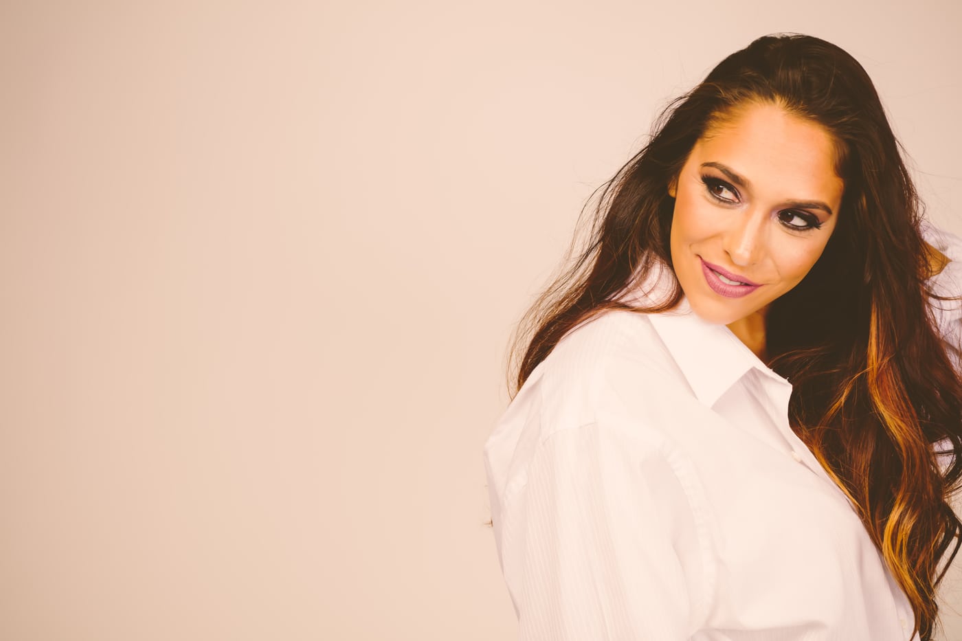 Woman white shirt, warm glam, hand in hair.