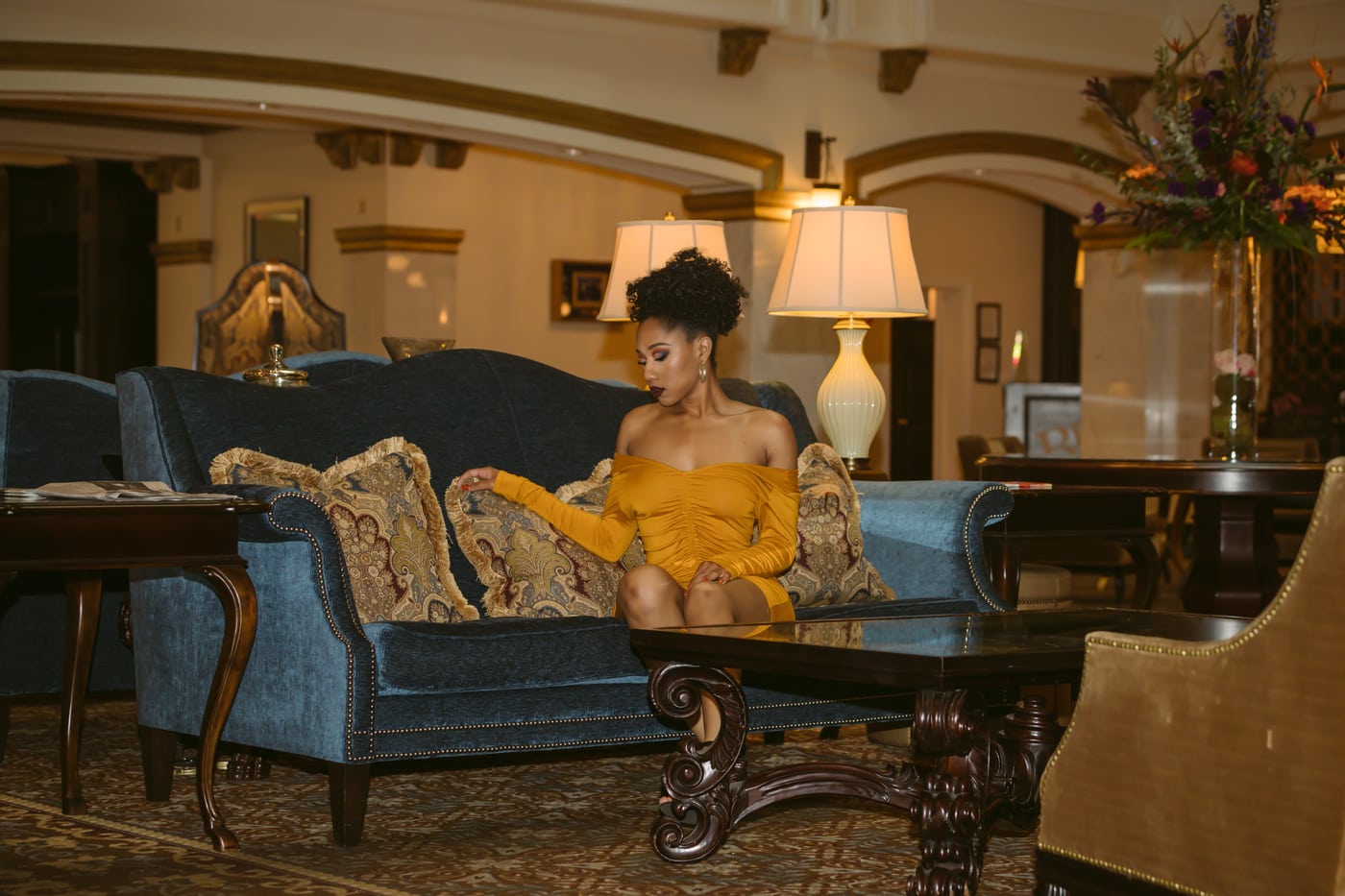 Woman yellow off-shoulder on antique sofa, luxe interior, fashion editorial.